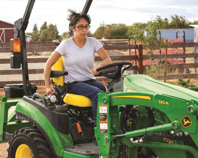 A homeowner uses a John Deere 1025R with a variety of attachments to maintain their home.