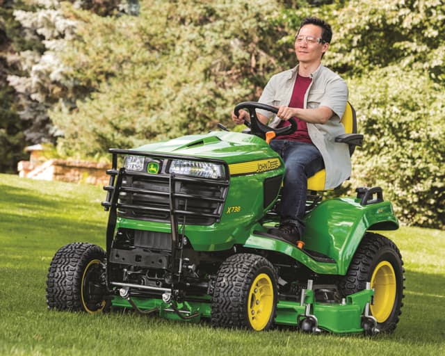 A man drives a John Deere X700 Series lawn mower.