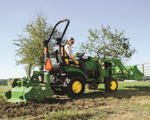 A property owner with a small tiller attachment tills the ground.