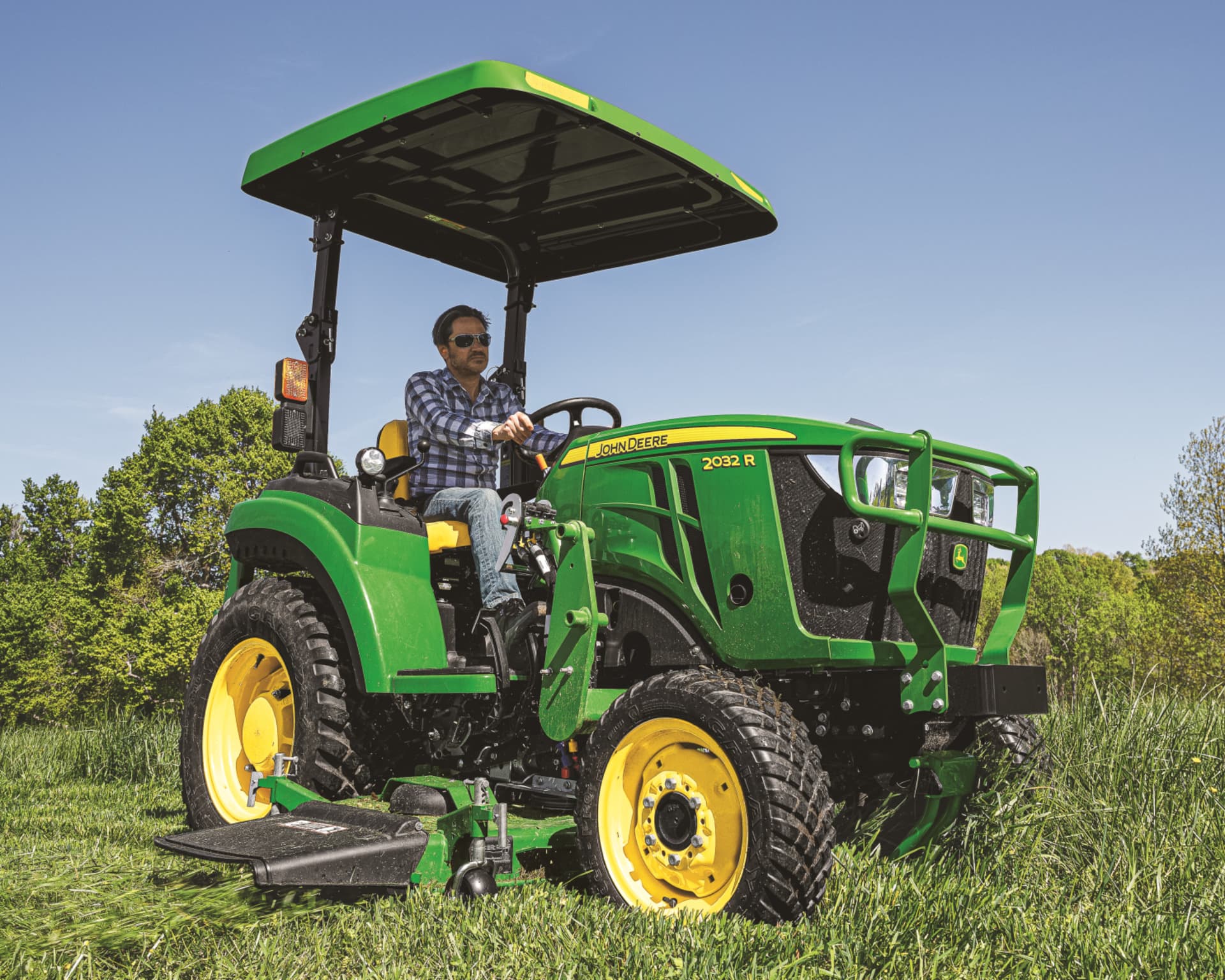 A John Deere 2032R compact tractor mowing a field.