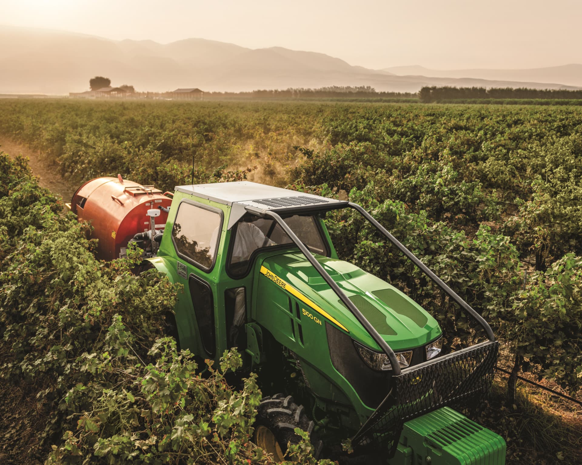 A sprayer attachment spraying a vineyard in California, pulled by a John Deere tractor.