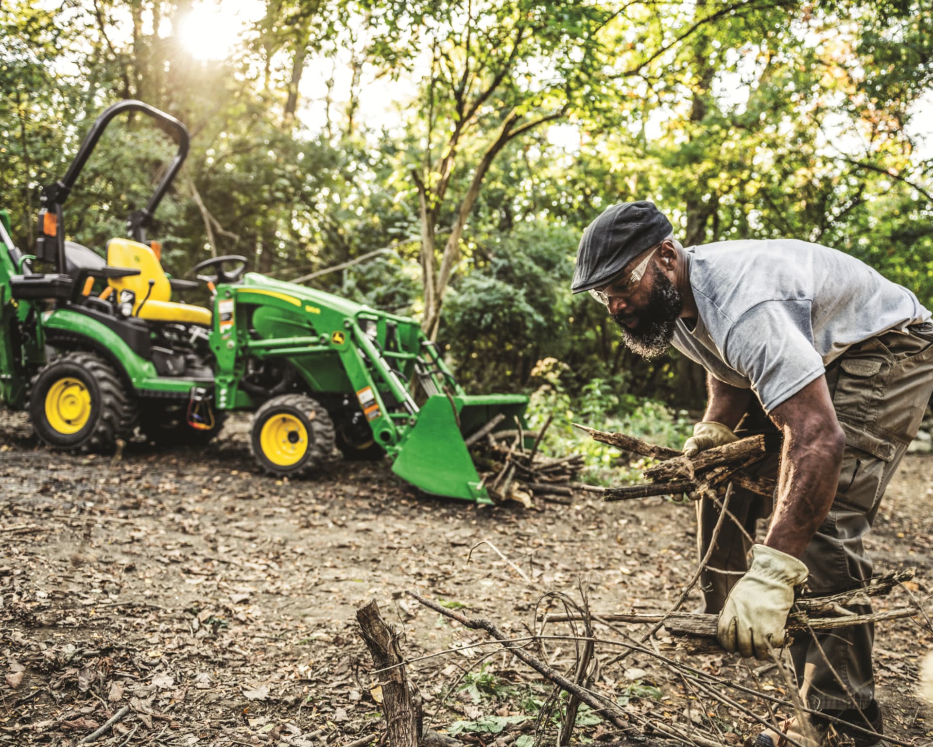 A property owner moves branches with the help of a John Deere 1025R with a front-end loader attachment.
