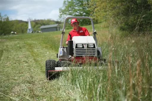 A worker uses a Ventrac Mower to maintain a grassy field on a property.
