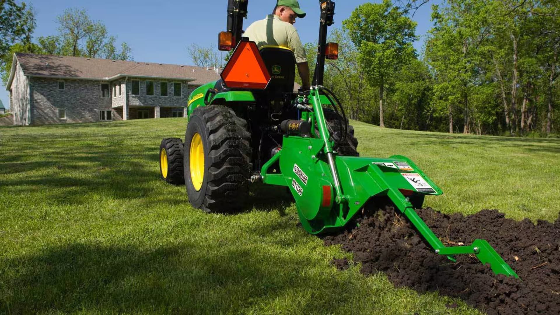 A man uses a ditching attachment to prep the ground for planting.