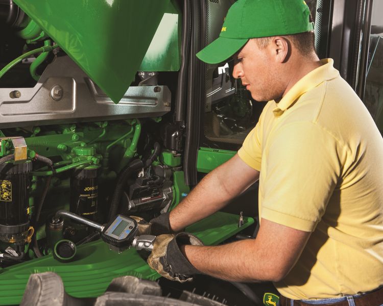 A technician changes the oil on a John Deere tractor.