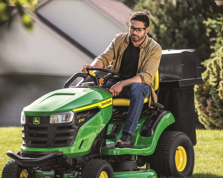 A homeowner mows their lawn with a John Deere lawn tractor.