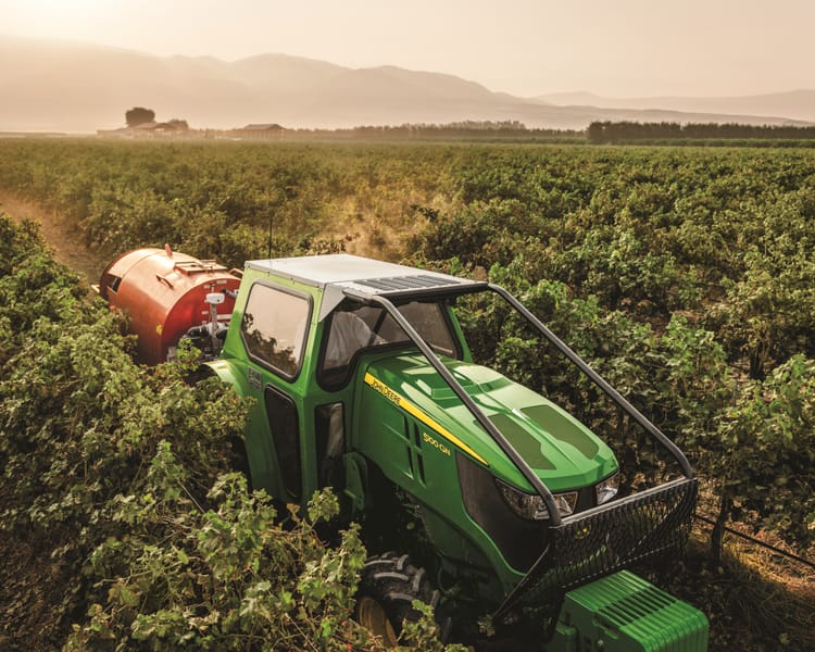 A sprayer attachment spraying a vineyard in California, pulled by a John Deere tractor.
