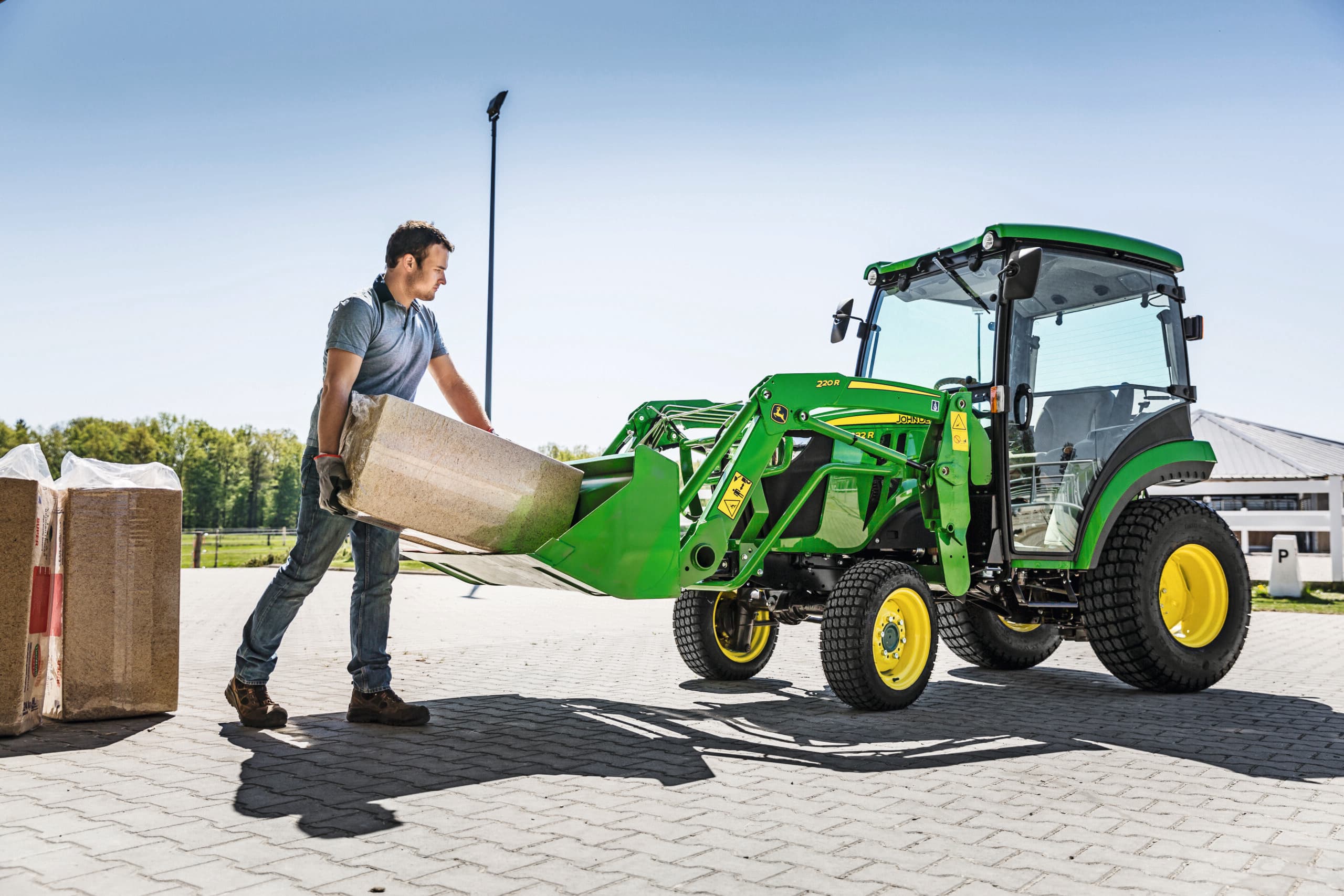 A man loads the front-end loader of a John Deere 2032R tractor.